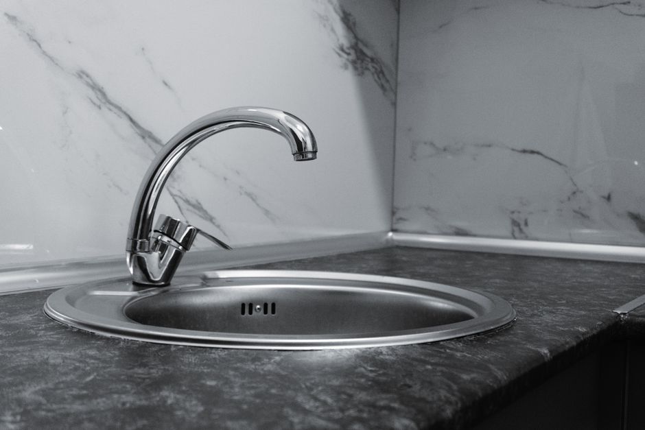 Stainless steel kitchen sink and faucet against marble backsplash in a modern kitchen.